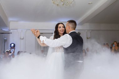 Bir çift, süslü bir salonda düğün töreninde dans ediyor. Misafirler oturur ve etraflarında dururlar, dans pistinin bir kısmını kaplayan sisin tadını çıkarırlar..