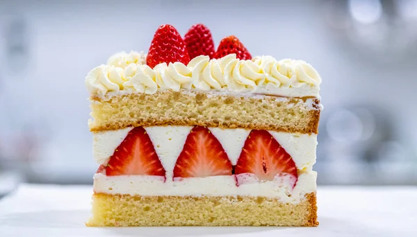 Lezzetli çilekli pasta diliminin yakın plan çekimi, nemli pasta katmanları, kremalı krema ve taze çilek dilimleri, üzeri canlı dutlarla kaplı..