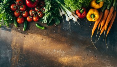 Koyu kırsal bir yüzeye yayılmış havuç, biber, domates, marul ve yeşillik gibi rengarenk sebzeler.