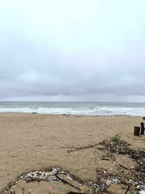 Doğu Malezya 'da muson mevsiminde kasvetli bir sahil sahnesi. Kara fırtına bulutları, güçlü dalgalar ve kumlu sahil boyunca dağılmış sürüklenen dallar ham ve dramatik sahil atmosferini yakalıyor..
