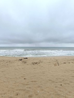 Doğu Malezya 'da muson mevsiminde kasvetli bir sahil sahnesi. Kara fırtına bulutları, güçlü dalgalar ve kumlu sahil boyunca dağılmış sürüklenen dallar ham ve dramatik sahil atmosferini yakalıyor..