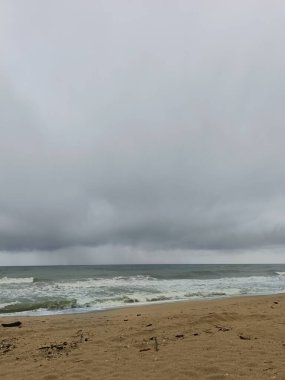 Doğu Malezya 'da muson mevsiminde kasvetli bir sahil sahnesi. Kara fırtına bulutları, güçlü dalgalar ve kumlu sahil boyunca dağılmış sürüklenen dallar ham ve dramatik sahil atmosferini yakalıyor..