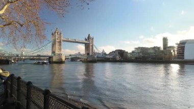 Londra 'da gün içinde Thames Nehri üzerindeki ikonik Tower Köprüsü manzarası. Su sakin ve köprünün altından küçük bir tekne geçiyor. Gökyüzü açık güneşli bir gün..