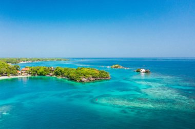 Cartagena, Kolombiya yakınlarındaki Islas del Rosario 'nun hava görüntüsü. Ada yoğun yeşil bitki örtüsüyle kaplıdır ve güneşli bir günde görünen mercan resifleri ve tekneleriyle turkuaz sularla çevrilidir..
