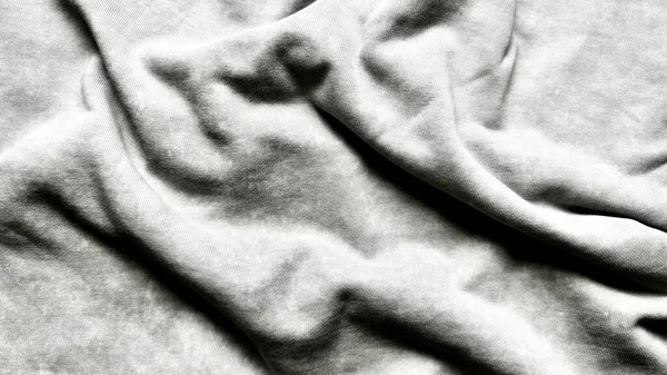 Usulca buruşmuş açık gri kumaşın makro dokusunu yakından çek. Kırışıklıkları nazik kıvrımlar ve ince gölgeler soyut minimalist.