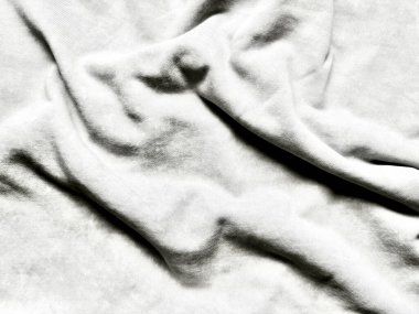 Kırışık beyaz kumaş kıvrımlarının tek renkli görüntüsü soyut dokuya yumuşak gölgeler bırakarak sükunet minimalizmi ve dokunsal derinliği çağrıştırıyor.