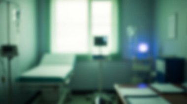 Tıbbi muayene odasının bulanık görüntüsü. Hastane yatağı, tıbbi gereçler ve yumuşak gün ışığına izin veren bir pencere..