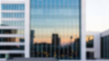 Parlak cam cepheli modern bir ofis binası ılık bir günbatımı gökyüzünü yansıtır..