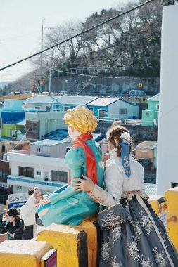 Şehre tepeden bakan renkli heykelin yanında oturan kız.