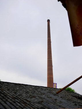 Çatıların üzerinde yükselen uzun tuğla baca.