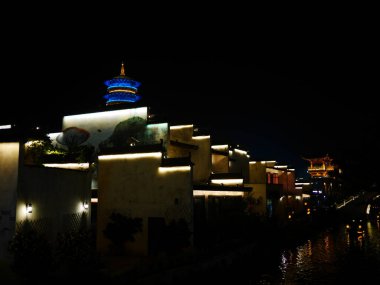 Gece karanlık su yolu boyunca aydınlatılmış binalar.