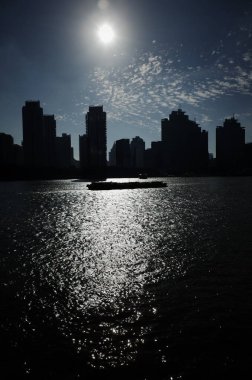 Siluetli binalar güneş ışığını suya yansıtıyor.