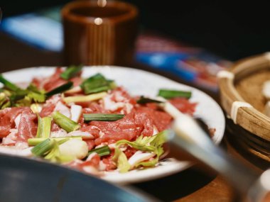 Dilimlenmiş et, yeşil soğanla süslenmiş.