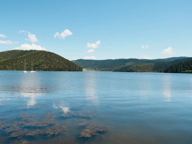Sakin göl mavi gökyüzünü ve tepeleri yansıtıyor
