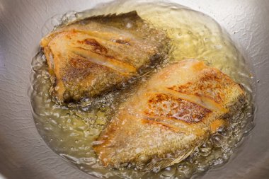 Tayland usulü yılan derisi gourami tavada kızgın yağla kızartılıyor, çıtır çıtır altın dokuları gösteriyor..