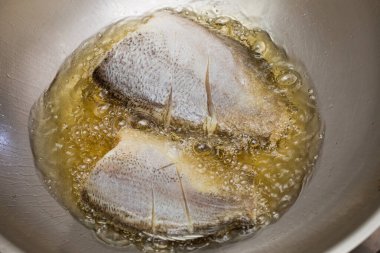 Tayland usulü yılan derisi gourami tavada kızgın yağla kızartılıyor, çıtır çıtır altın dokuları gösteriyor..