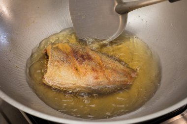 Tayland usulü yılan derisi gourami tavada kızgın yağla kızartılıyor, çıtır çıtır altın dokuları gösteriyor..
