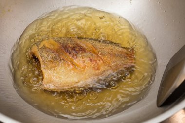 Tayland usulü yılan derisi gourami tavada kızgın yağla kızartılıyor, çıtır çıtır altın dokuları gösteriyor..