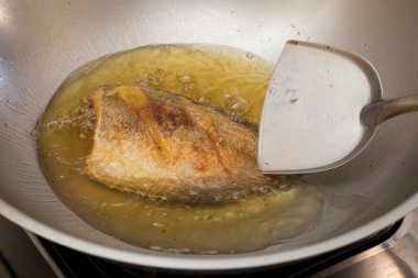 Tayland usulü yılan derisi gourami tavada kızgın yağla kızartılıyor, çıtır çıtır altın dokuları gösteriyor..