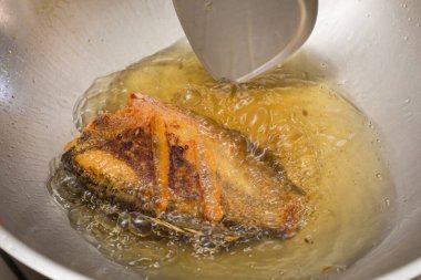 Tayland usulü yılan derisi gourami tavada kızgın yağla kızartılıyor, çıtır çıtır altın dokuları gösteriyor..