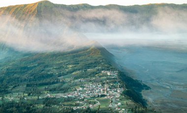 Sabah sisli, yemyeşil dağlara kurulmuş bir köy. Yuvarlanan yeşil tepeler ve dağlarla çevrili küçük bir köyün havadan görünüşü, kısmen sabah sisi ile gizlenmiş. Sıcak, farklı..