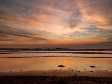 Renkli Gökyüzü ile Ocean Beach 'te Günbatımı. Sıcak, altın saat ışıklandırması. Gün batımını yansıtan sakin dalgalar. Dramatik, çizgili bulutlar. Huzurlu ve huzurlu bir ortam. Yatay bileşim.