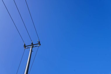 Clear Blue Sky 'a karşı güç hatları. Elektrik direğinin alçak açılı çekimi ve elektrik hatları canlı, bulutsuz mavi gökyüzüne karşı. Parlak, doğal ışıklandırma. Minimalist estetik.