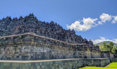 Borobudur Tapınağının dışı, Java, Endonezya. Parlak gün ışığı antik taş yapıyı aydınlatır. Tüylü bulutlarla dolu açık mavi gökyüzüne karşı tapınak katlarını detaylı oymalar kaplıyor. Lus.