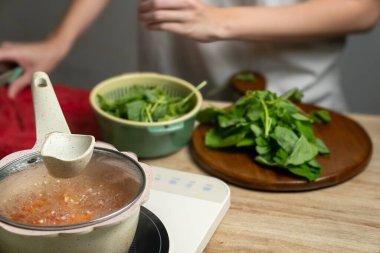 Taze Ispanak Hazırlama: Yemek ve Doğrama Malzemeleri. Yakın çekim, alan derinliği. Sıcak, doğal ışıklandırma. Kırsal ahşap masa. Tencere ve ıspanağa odaklan. Yumuşak, soluk renk.