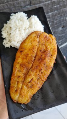 Kızarmış muz ve siyah tabakta beyaz pirinç. Pürüzsüz, siyah dikdörtgen bir tabakta servis edilen, altın kızartılmış muz ve kabarık beyaz pirinçten yakın çekim. Sıcak ışıklandırma, basit kompozit.