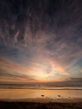 Ocean Beach 'te dramatik bir gün batımı, Altın Saat. Gün batımında sahilin geniş açılı görüntüsü. Dramatik, desenli bulutlar gökyüzünü turuncu ve mor renklerle dolduruyor. Islak kumda yansımalar.