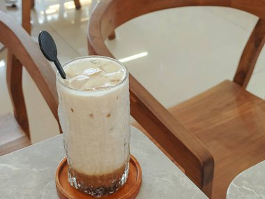 Buzlu Kaşık ve Kaşık, Cafe Setting. Parlak, dokulu bir bardak buzlu kahvenin doğal ışıklandırması. Koyu kahve tabanıyla görülebilen kremalı tabakalar. Tahta kaşık ve bardak altlığı. Yumuşak, inv.