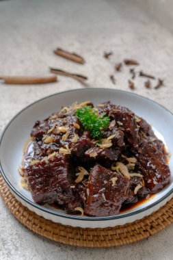 Beef Rendang Curry White Bowl 'da servis ediliyor. Yakın plan, zengin, koyu etli rendang köri kalıplı bir kasede. Taze otlar ve tarçın çubuklarıyla süslenmiş. Sıcak, davetkar çakmak..