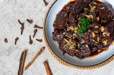 Baharatlı Beef Rendang Curry: Genel Görünüm. Koyu, zengin köri körisi taze otlarla süslenmiş desenli bir tabakta sunuluyor. Sıcak, davetkar bir ışık ve sığ bir alan derinliği.