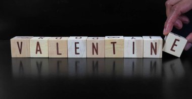 VALENTINE kelimesi, siyah bir arka planda izole edilmiş ahşap bloklardan oluşan harflerden oluşur..