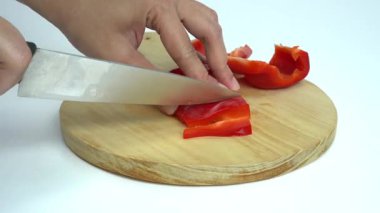 Bir kadın kırmızı bir dolma biberin ya da kırmızı biberin vücudunu kibrit çöpü gibi boydan boya kesiyor, yuvarlak kahverengi bir tahta kesme tahtasında, beyaz bir arka planda izole edilmiş.