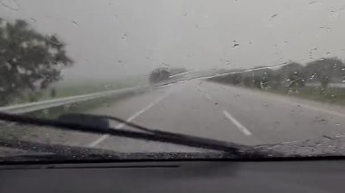 Araba ön camındaki yağmur damlalarının giderilmesi araba tenha bir yolda giderken araba silecekleri tarafından temizleniyor.