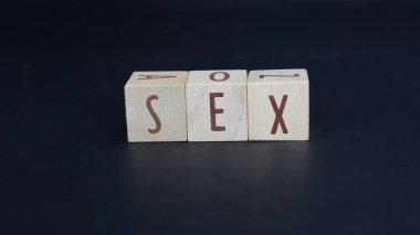 SEX kelimesi, siyah bir arkaplanda izole edilmiş, tahta bloklardan oluşan harflerden oluşur..