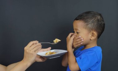 Küçük bir Asyalı erkek çocuğu iki eliyle ağzını kapatıyor, GTM (Kapalı Ağız Hareketi) olarak bilinen ve kendisini kaşıkla besleyen annesinden yemeye devam etmek istemeyen bir jest. Bebek bakımı kavramı