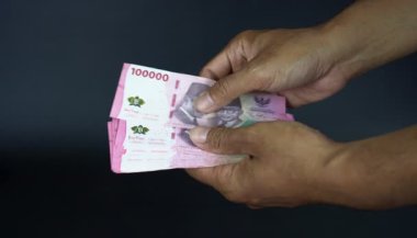 Asyalı bir adam yüz bin rupiah banknot sayıyor bulanık bir konsept, temalı finans, hesaplı maaş, gelir, nakit ödeme, siyah bir arka planda izole