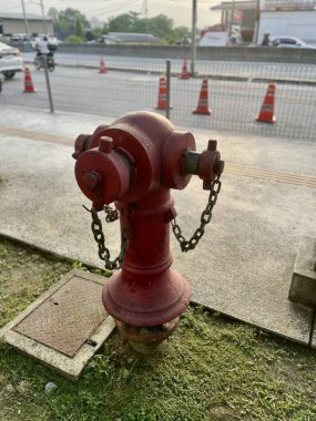 Şehir caddesinde trafik konilerinin ve araçların yanında zincirli kırmızı yangın musluğu ve hortumu var.