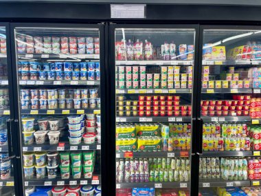 Kuala Lumpur, Malezya - 6 Aralık 2025: Bir süpermarket koridorunda renkli yoğurt ve süt ürünleri sıralarını gösteren soğutulmuş cam kapıların tam görünümü