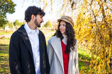 Romantik bir parkta yürürken birbirlerine sevgiyle bakan genç bir çift.