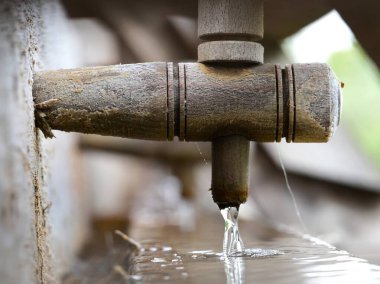 Taze suyla dolu eski bir ahşap oluğun yakın çekimi. Usulca yalağa akıyor, kırsal dokuları ve doğal işçiliği sergiliyor.
