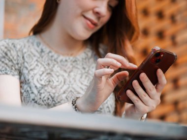 Sırt çantası ve kulaklıklı genç bir kadın parkta akıllı telefondan mesaj atarken gülümsüyor, öğrenci ya da serbest çalışan cep telefonu teknolojisi ve internet iletişimi kullanıyor..