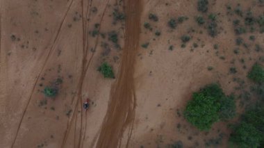 Bir off-road motosikletlinin kumlu arazide birden fazla lastik izi olan tepeden aşağı hava görüntüsü. Güçlü dokusu ve negatif alanı olan, macera, yarış ve keşif kavramları için ideal, ücra bir motor sporu sahnesi..