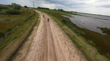 Bataklıklar ve su arasında dar bir toprak yol boyunca giden bir grup off-road motosikletlinin hava aracı görüntüsü. Uzak doğadaki açık hava macera konvoyu, seyahat, keşif ve dayanıklılık için ideal..