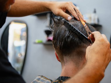 Bir berber, berber dükkanında makas ve tarak ile çalışırken, bir adamın saçını kestirirken ki arka plan görüntüsü, gerçek bir tımar rutini ve şekle ve detaylara dikkat göstermektedir..