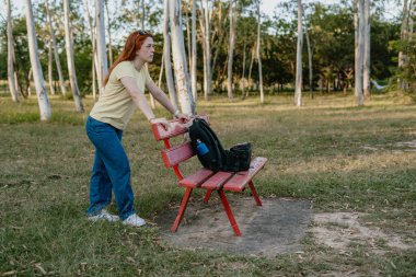 Bir yetişkin, sırtında bir sırt çantası taşırken kırmızı bir bankı hareket ettirir. Değişimi, karar vermeyi ve günlük esnekliği simgeler..