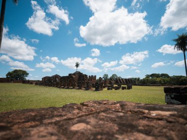 Arka planda bulutlu mavi bir gökyüzünün altında eski harap yapılar olan bir çim tarlasının yatay manzarası. Turizm, tarih, miras, kültür, varış yerleri ve seyahat içeriği için kullanışlı.